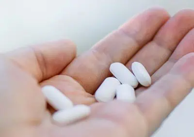 A person's hand holding several white oval-shaped pills.