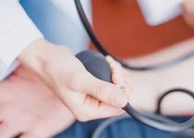 A healthcare professional holds a blood pressure cuff around a patient's arm, preparing to measure their blood pressure.