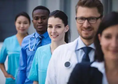 A group of healthcare professionals standing in a line and smiling, with a mix of nurses and doctors in blue and white uniforms.