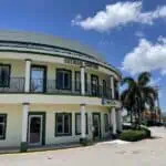 Two-story building labeled "Cayman Center" on a sunny day, with clear blue sky and palm trees. The building has green accents and a tiled roof.