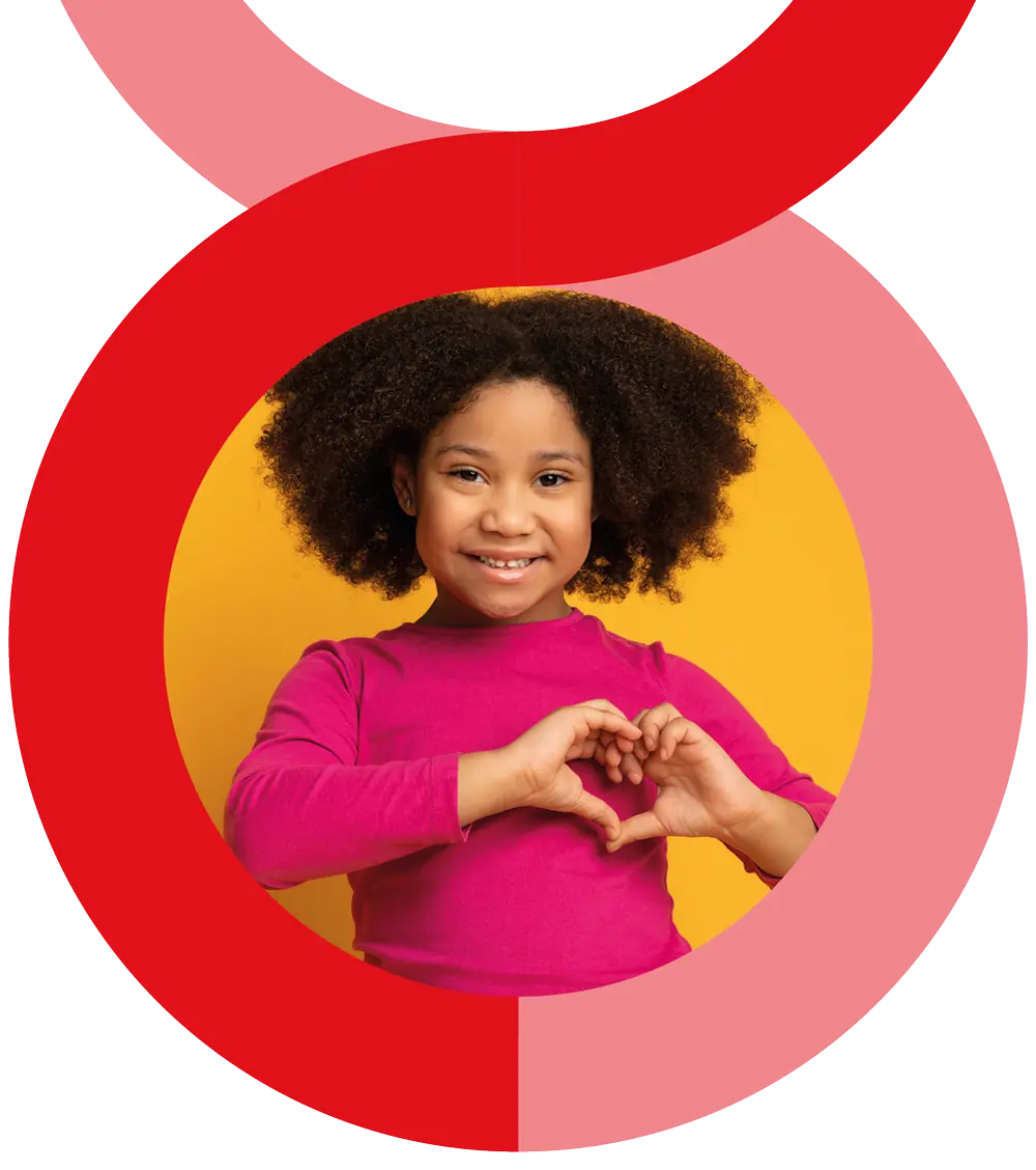 A young girl with curly hair and wearing a pink long-sleeve shirt forms a heart shape with her hands against a yellow background.