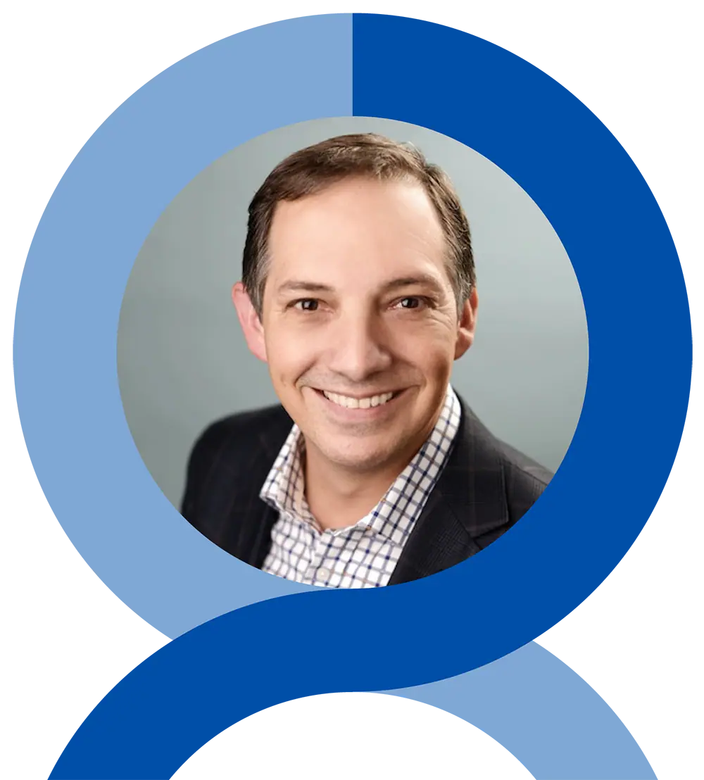 A man with short brown hair and a plaid shirt smiles at the camera in a professional headshot, framed by a blue circular graphic.