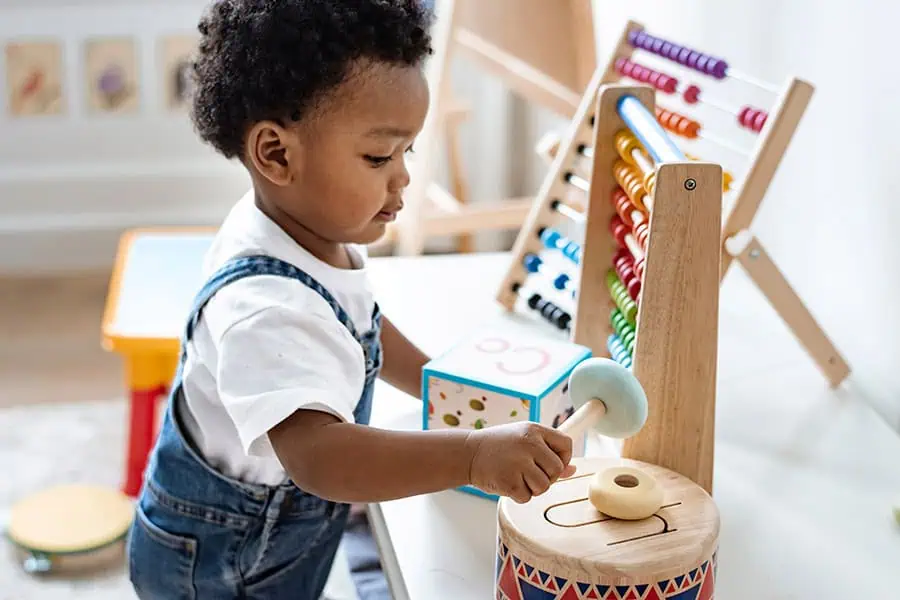 Child playing with educational toys, including an abacus and a drum, in a brightly lit room.