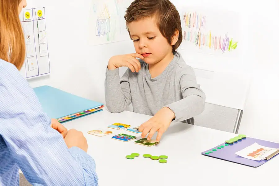 Child playing a card game at a table with an adult. Crayons and artwork in the background.