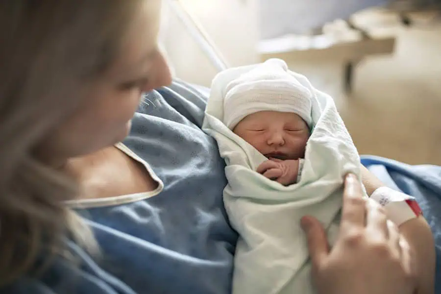 A person holding a newborn baby wrapped in a blanket, both in a hospital setting.