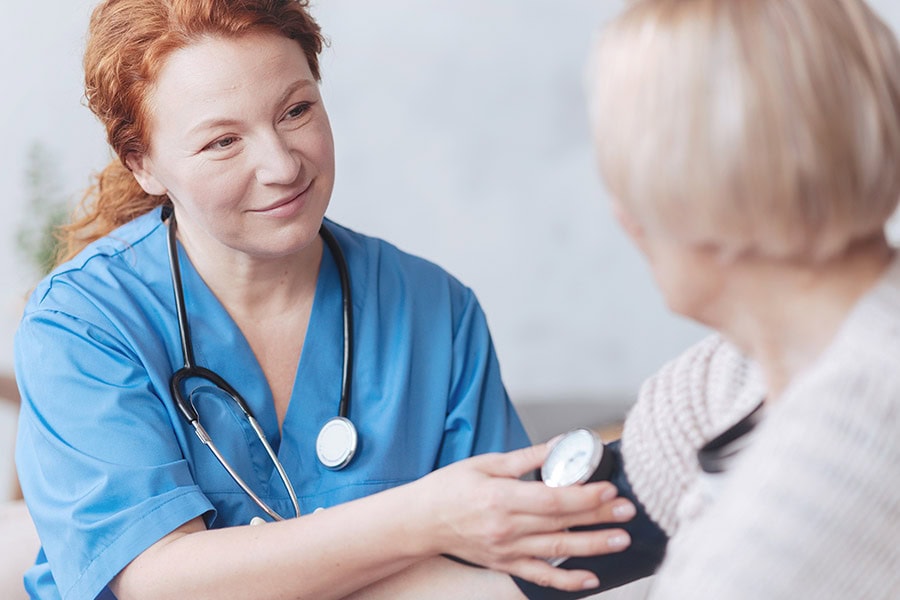 A nurse in blue scrubs checks the blood pressure of an older woman during a medical appointment.